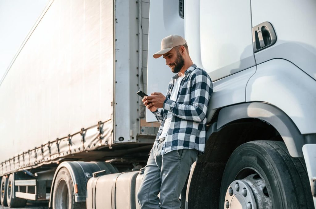 truck driver leaning by his vehicle and using phone