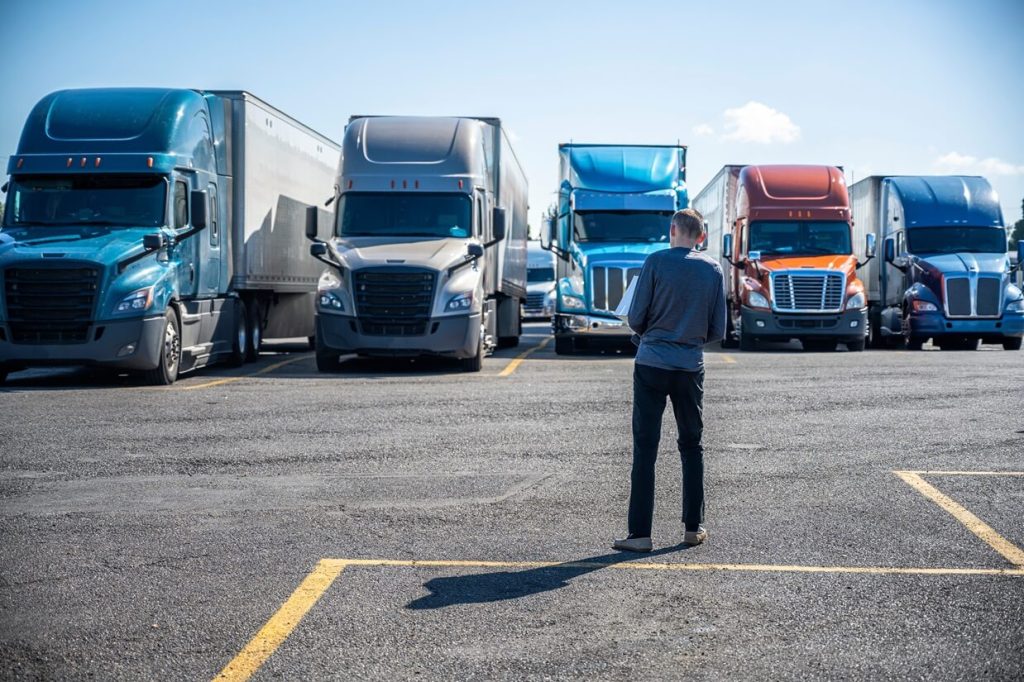 Truck driver carries a shopping box in his hands and goes to his big rig semi truck parked on the truck stop parking lot